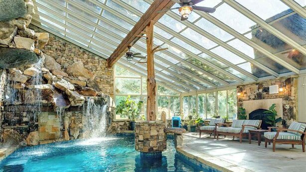 Una piscina interior con cascada, paredes de piedra y mobiliario de madera.