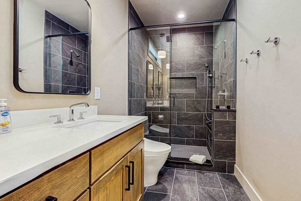 Un baño moderno con un espejo grande, un lavabo blanco, un inodoro y una zona de ducha con mampara de vidrio.