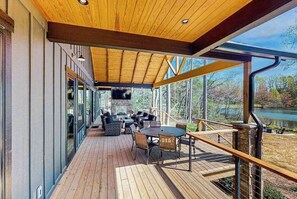 Eine Holzterrasse mit Gartenmöbeln, einem Kamin und Blick auf einen See.