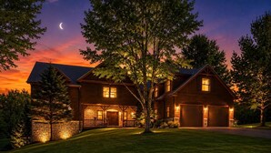 A two-story house with a stone foundation, a large front porch, and a garage. - 4BR | Pool Table + Foosball | (Apple River)