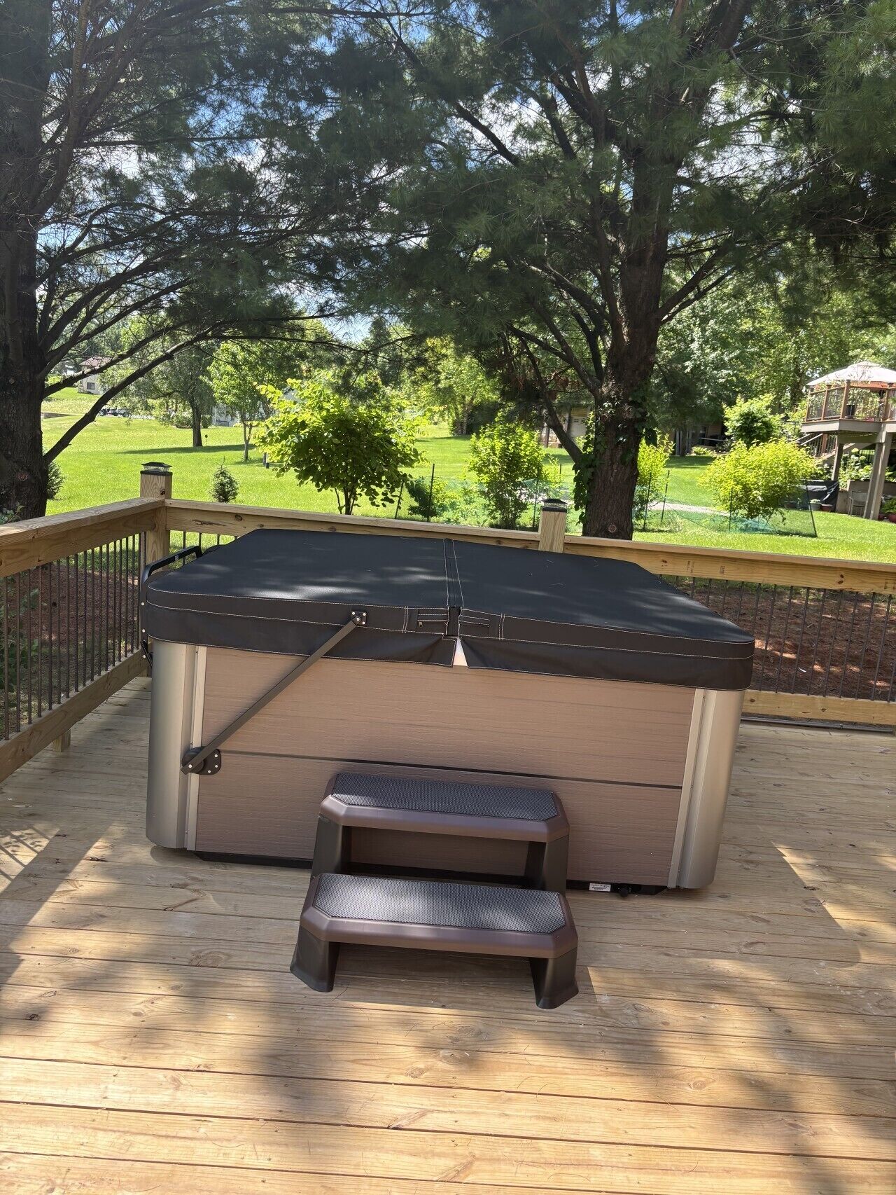 A hot tub on a wooden deck with a view of a grassy yard and trees.