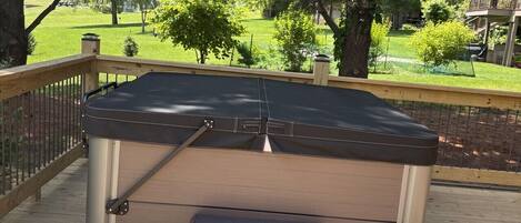 A hot tub on a wooden deck with a view of a grassy yard and trees.