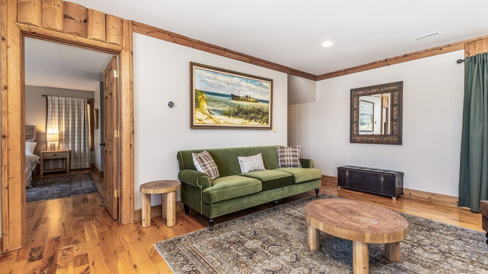 A cozy living room with a green sofa, a round wooden coffee table, and a painting on the wall.