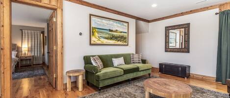A cozy living room with a green sofa, a round wooden coffee table, and a painting on the wall.