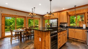 A kitchen with wooden cabinets, a central island, and a dining area with a table and chairs. - 4BR | Pool Table + Foosball | (Apple River)