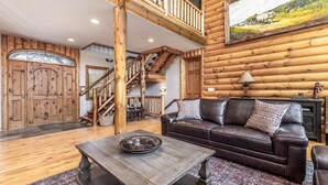 A rustic interior with a wooden staircase, leather sofa, and a dining table. - 4BR | Pool Table + Foosball | (Apple River)