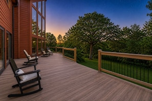 A wooden deck with outdoor seating and a view of trees and a sunset.