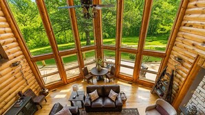 A log cabin interior with a large glass window, a leather sofa, a round table, and a chair. - 4BR | Pool Table + Foosball | (Apple River)