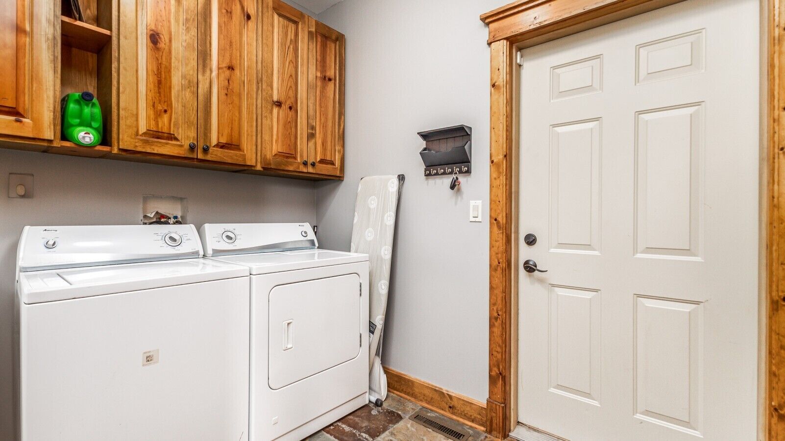 A laundry area with two washing machines, wooden cabinets, a white door, and a small black mailbox.