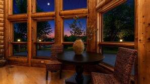 Un interior de madera con ventanas amplias, una mesa redonda, sillas de mimbre y un florero.