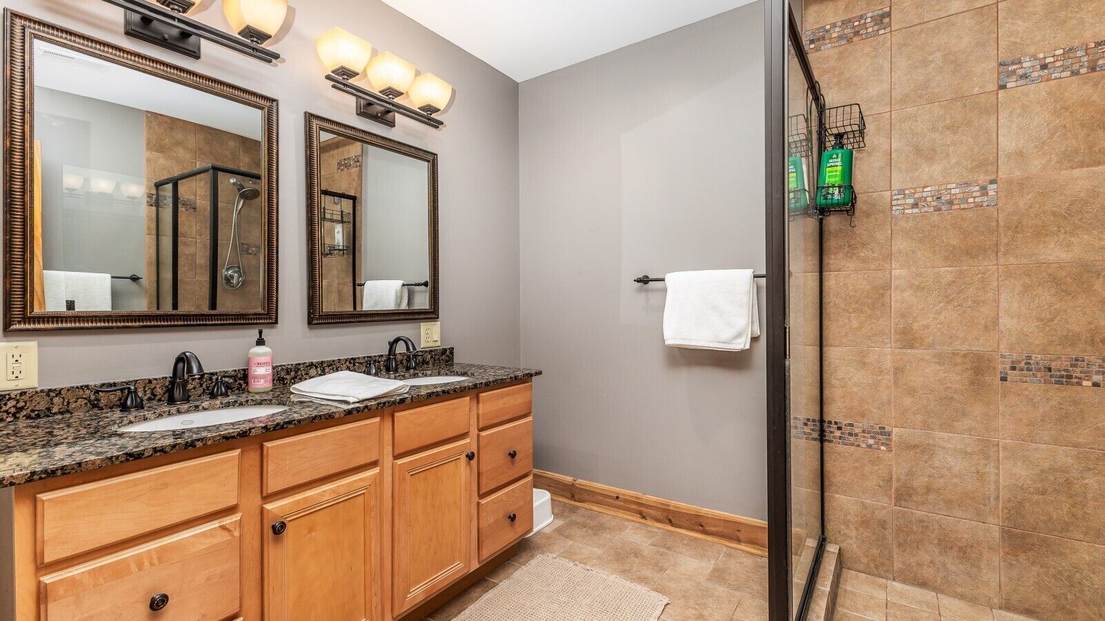 Une salle de bain avec deux lavabos, des meubles en bois, un grand miroir et un espace douche.