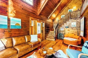 Ein Holzblockbau-Innenraum mit einer Couch, einem Sessel, einer Treppe und Holzboden.