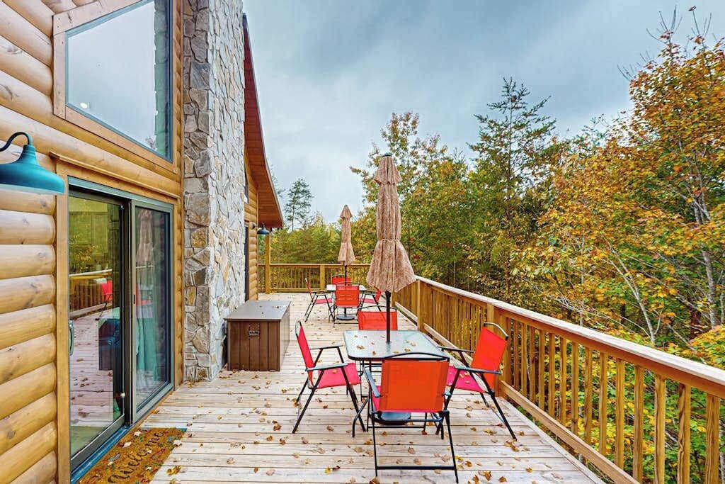 A wooden deck with outdoor seating, stone walls, and a view of autumn foliage.