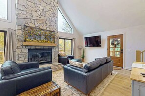 Ein geräumiges Wohnzimmer mit Kamin aus Stein, Ledersofas und einem wandmontierten Flachbildfernseher.
