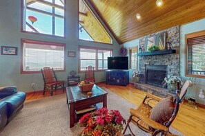 A cozy living room with a fireplace, a television, and a stone wall. - Amazing  Pet Friendly chalet w/ mountain views, wraparound porch, & hot tub (Murphy)