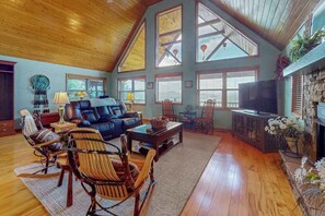 A spacious living room with a high ceiling, large windows, a fireplace, and a television. - Amazing  Pet Friendly chalet w/ mountain views, wraparound porch, & hot tub (Murphy)