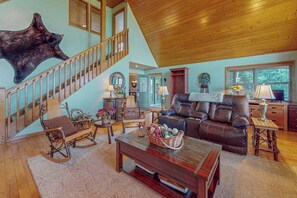 A spacious living room with a wooden staircase, a leather sofa, and a large wall-mounted animal head. - Amazing  Pet Friendly chalet w/ mountain views, wraparound porch, & hot tub (Murphy)