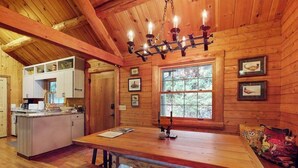 A wooden cabin interior with a dining table, bench, kitchen area, and a chandelier. - Dog-Friendly with Hot Tub & Fire Pit Overlooking Golf Course at Lake Toxaway (Lake Toxaway)