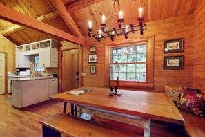 Ein Holzblockhaus-Interieur mit Esstisch, Bank, Küchenbereich und einer Chandelüster.