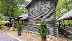 A log cabin with a stone-paved entrance, two potted evergreen trees, and a covered porch. - Dog-Friendly with Hot Tub & Fire Pit Overlooking Golf Course at Lake Toxaway (Lake Toxaway)