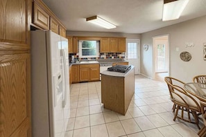 A kitchen with wooden cabinets, a refrigerator, a stove, and a dining area with a table and chairs. - Warm & inviting upper-level guest suite w/ deck, shared washer/dryer, central AC (Candler)