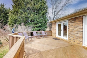 A deck with chairs and a table, a brick wall, and a large tree. - Warm & inviting upper-level guest suite w/ deck, shared washer/dryer, central AC (Candler)