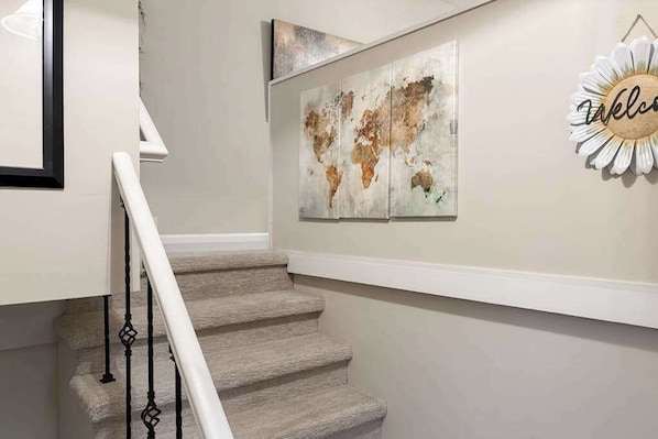 A staircase with a white railing, a world map artwork on the wall, and a 'Welcome' sign. - Warm & inviting upper-level guest suite w/ deck, shared washer/dryer, central AC (Candler)