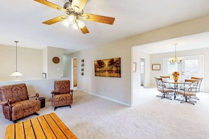 A living room with two patterned sofas, a wooden coffee table, a dining area with a table and chairs, a ceiling fan, and a painting on the wall. - Warm & inviting upper-level guest suite w/ deck, shared washer/dryer, central AC (Candler)