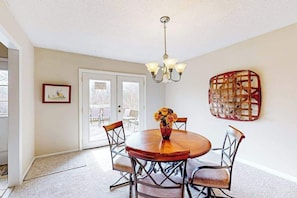 A dining area with a round wooden table, four chairs, a vase with flowers, a chandelier, and a large abstract art piece on the wall. - Warm & inviting upper-level guest suite w/ deck, shared washer/dryer, central AC (Candler)