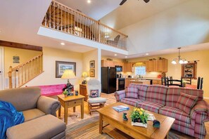 A spacious living room with a sofa, a coffee table, and a dining area with a table and chairs. A kitchen is visible in the background. - Carr House Upper (Lake Junaluska)