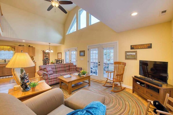 A spacious living room with a high ceiling, a fireplace, a television, and a dining area. - Carr House Upper (Lake Junaluska)