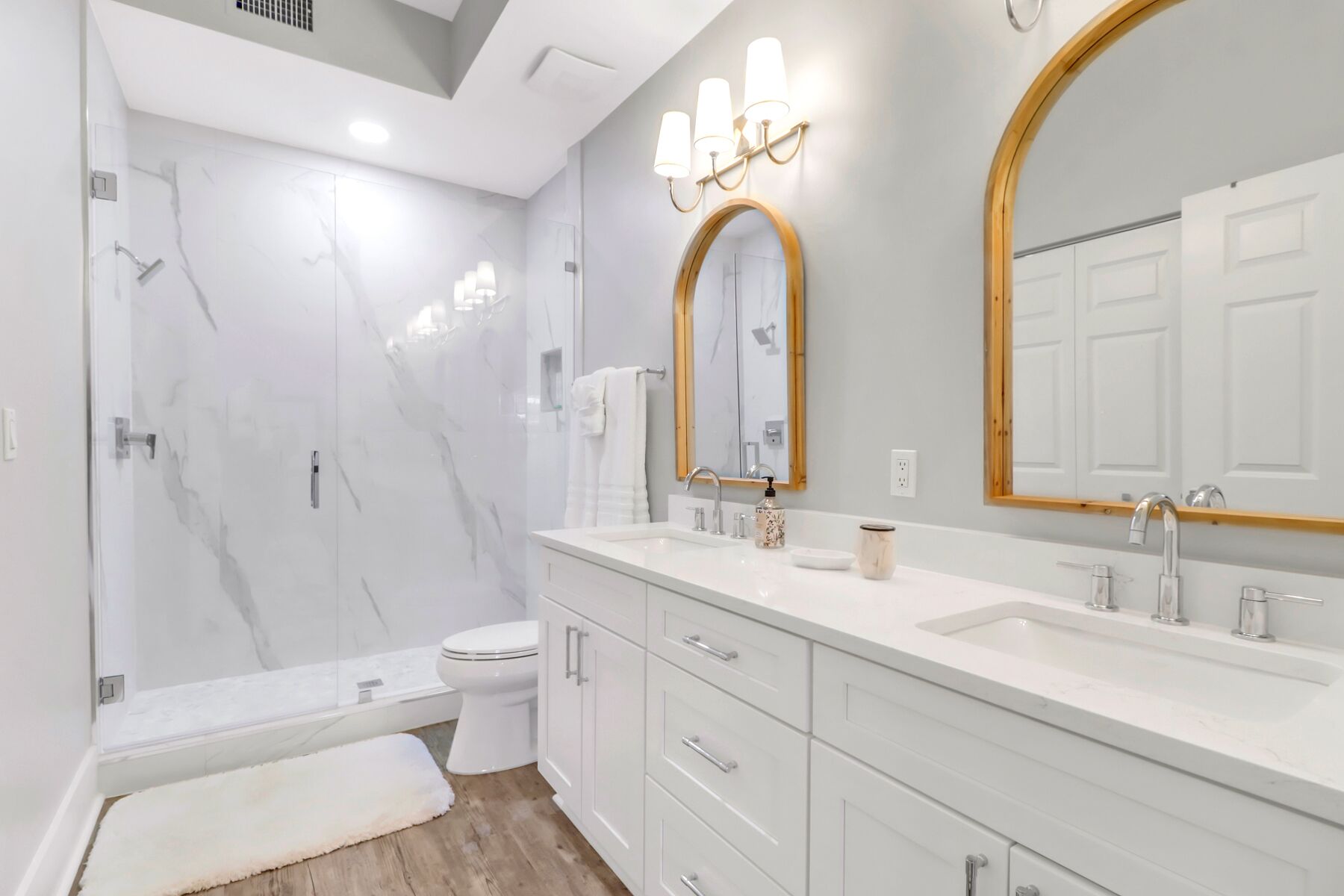 A modern bathroom with a shower, toilet, vanity, and two large mirrors.