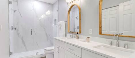 A modern bathroom with a shower, toilet, vanity, and two large mirrors.