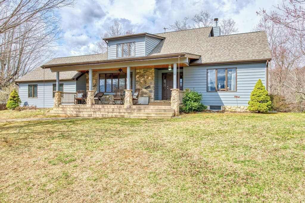 A two-story house with a covered porch, stone pillars, and a stone foundation.