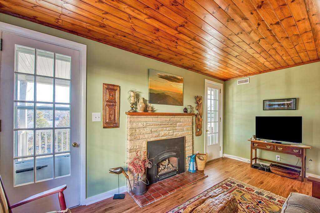 A living room with a fireplace, wooden ceiling, and a television on a stand.