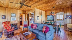 A wooden-paneled room with a sofa, armchair, dining table, and ceiling fan. - Hearthside at Lake Junaluska (Lake Junaluska)