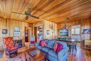 A wooden-paneled room with a sofa, armchair, dining table, and ceiling fan. - Hearthside at Lake Junaluska (Lake Junaluska)