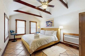 A bedroom with a bed, a ceiling fan, two windows, a chair, a painting, a lamp, and a radiator. - Charming Brevard cottage perfect for a getaway with local shops & breweries! (Brevard)