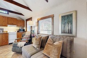 A cozy living room with a sofa, a chair, wooden cabinets, a kitchen area, and a window with blinds. - Charming Brevard cottage perfect for a getaway with local shops & breweries! (Brevard)