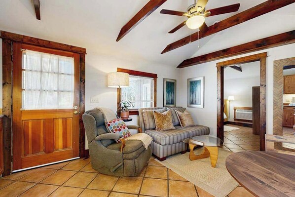 A living room with a sofa, armchair, and coffee table, wooden beams on the ceiling, and a door with a window. - Charming Brevard cottage perfect for a getaway with local shops & breweries! (Brevard)