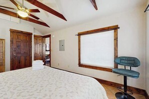 A bedroom with a bed, a ceiling fan, wooden beams, a window with blinds, and a bar stool. - Charming Brevard cottage perfect for a getaway with local shops & breweries! (Brevard)