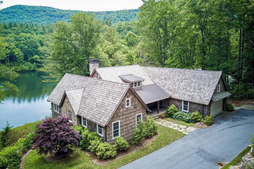 A house with a stone exterior, multiple gabled roofs, and a driveway leading to a garage.