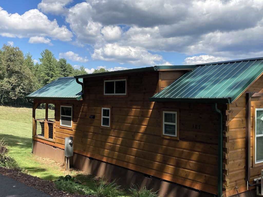 A wooden cabin with a green metal roof, a small porch, and a window.