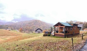 A wooden cabin with a porch, surrounded by a fenced yard and a mountain backdrop. - Scenic Cabin w/ Private Hot Tub, Amazing Views, & Covered Porch. Nearby Skiing (Mars Hill)