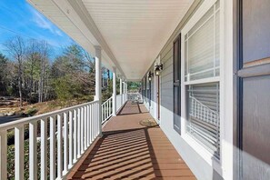 A covered porch with a wooden deck, white railings, and a view of trees and a road. - Mountain Ranch Home w/ Pool Table, Fire Pit & Porch Rockers (Hendersonville)