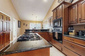 A kitchen with wooden cabinets, a central island with a stove, a microwave, and a coffee maker. - Mountain Ranch Home w/ Pool Table, Fire Pit & Porch Rockers (Hendersonville)