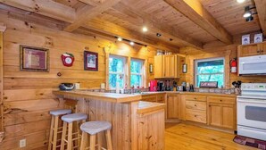 Ein Holzblockhaus-Interieur mit einer Küche, Barhocker und einer Mikrowelle.