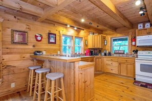 Ein Holzblockhaus-Interieur mit einer Küche, Barhocker und einer Mikrowelle.