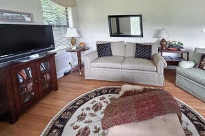 Ein Wohnzimmer mit einer Couch, einem Fernseher, einem Holzschrank und einem gemusterten Teppich.