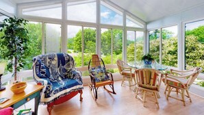 A conservatory with a glass table, wicker chairs, and a rocking chair with a patterned blanket. - Vintage charmer in Lake Junaluska with mountain views, pool & sunroom (Lake Junaluska)